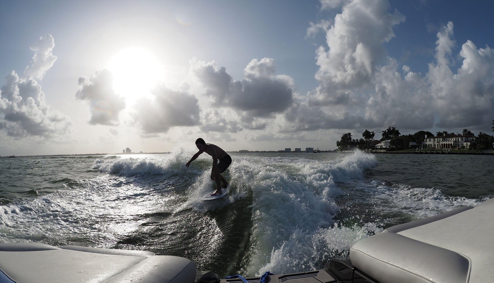 Man on wakeboard surfing the wake behind a boat on a lake on a sunny day.