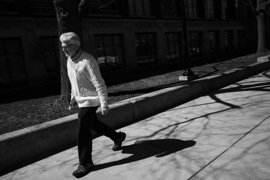 Black and white photo of an elderly professorial looking man walking on a college campus.