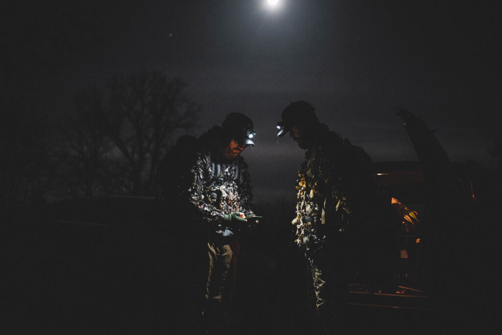 Two hunters conversing at night under the light of their headlamps.