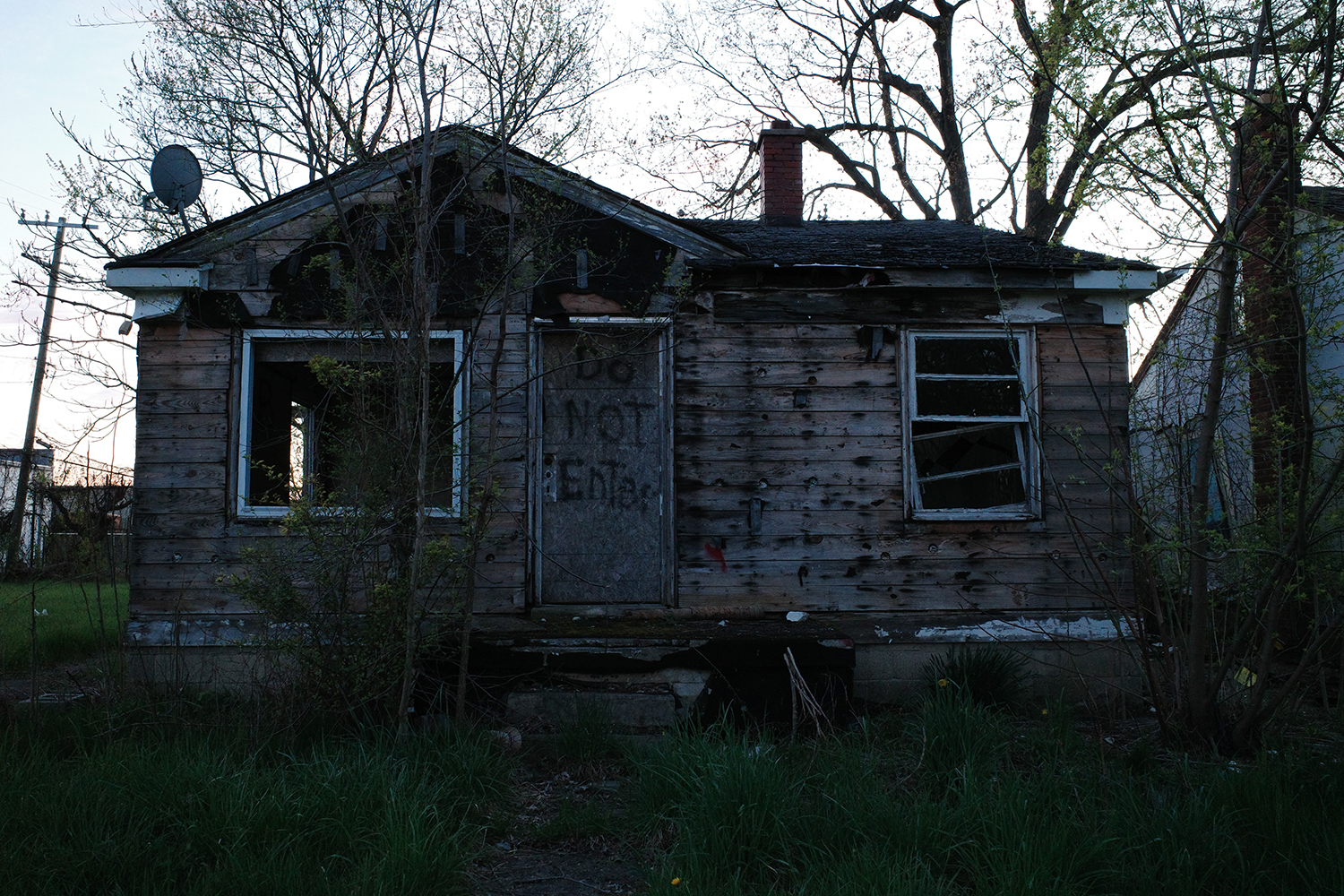 Abandoned home with broken windows and “Do Not Enter” spray painted on boarded up front door.