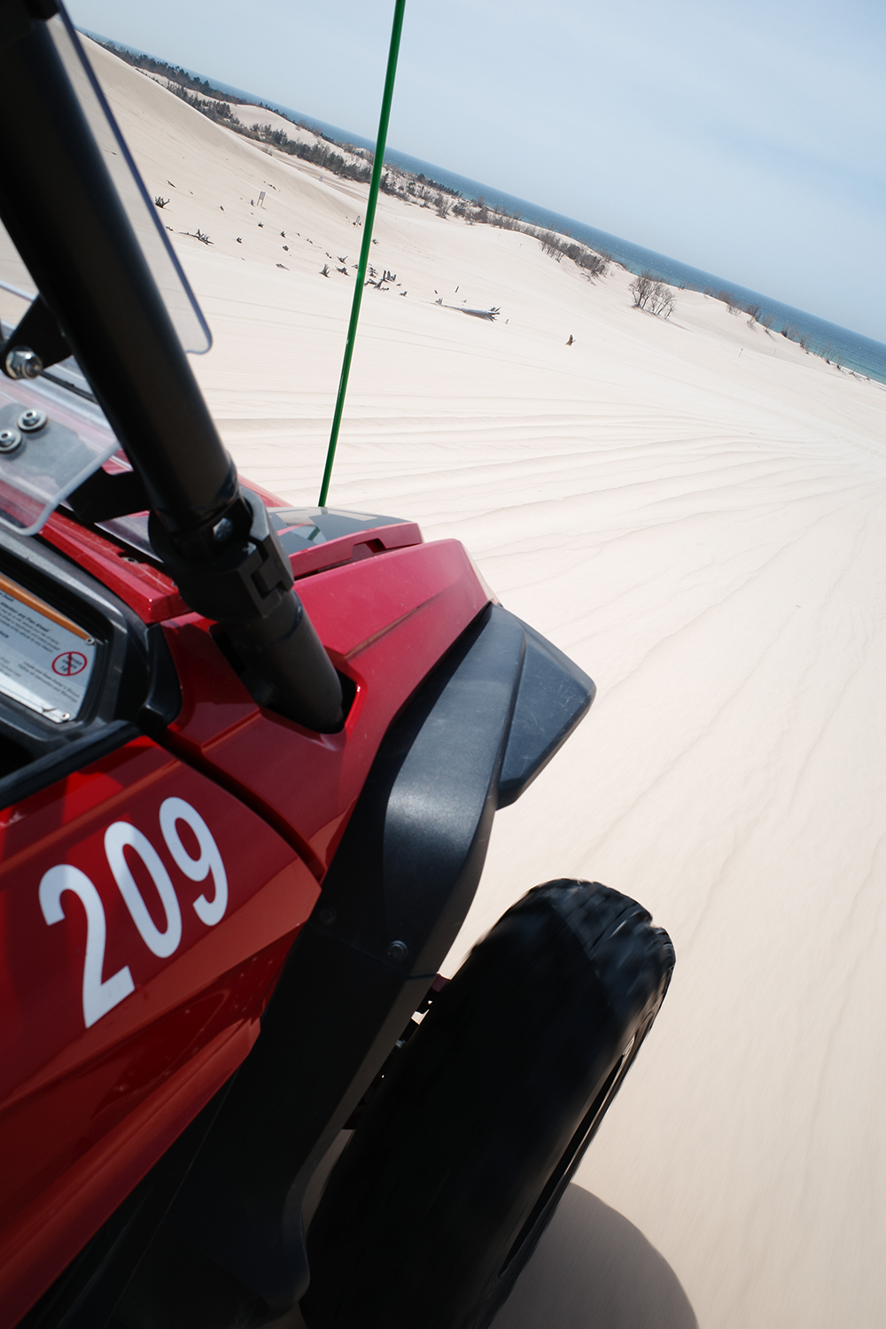 Side view of red dune buggy racing across a sand dune towards Lake Michigan.