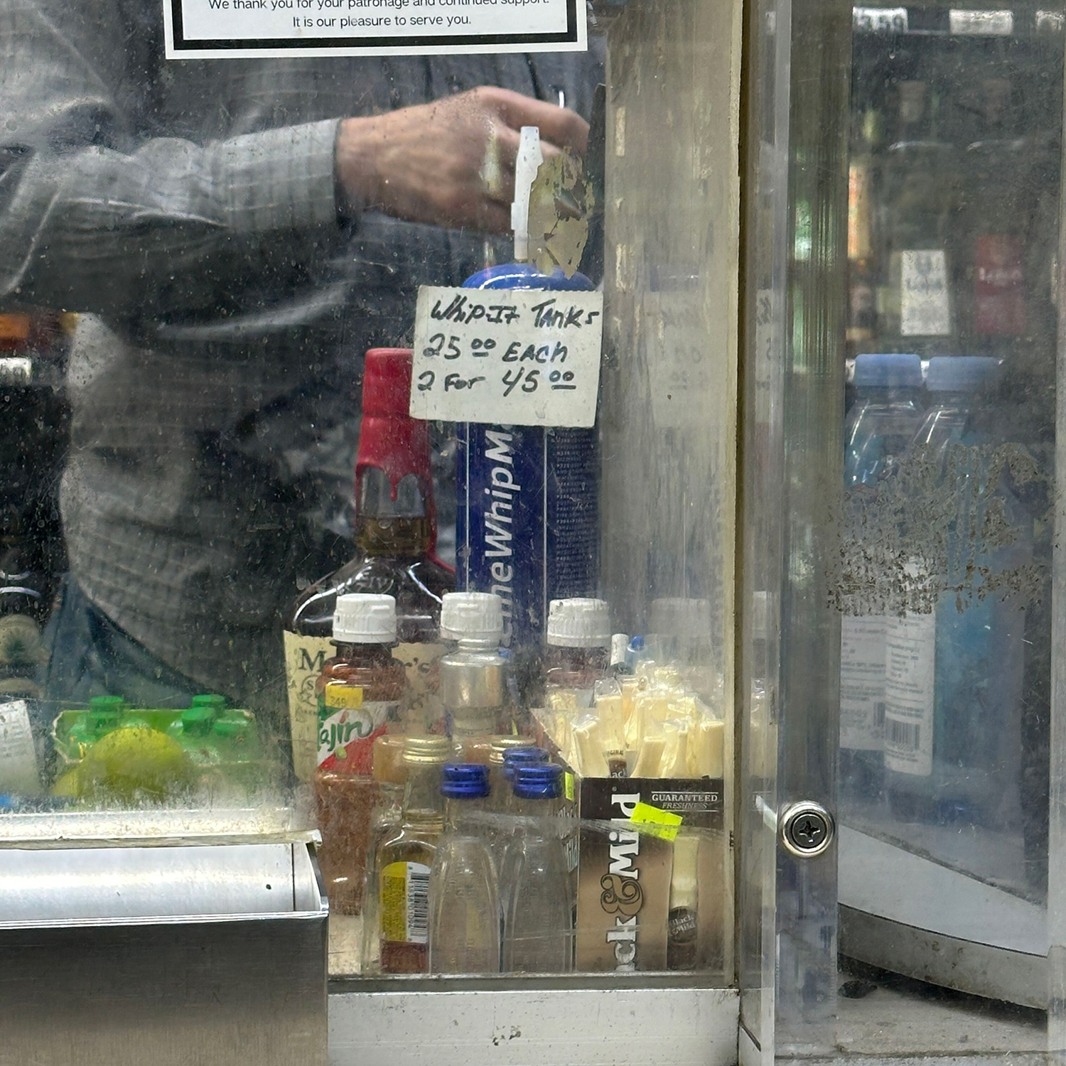 Whip-It tank behind glass on counter at liquor store, next to liquor bottles, with sign reading “Whip-It Tanks 25 dollars each, two for 45 dollars.”