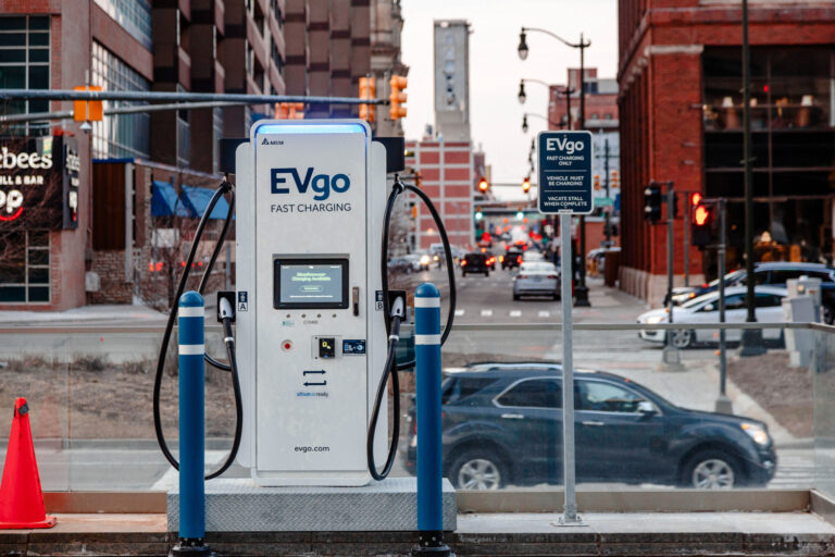 EV GO electric vehicle charging station in Detroit with cars passing by. Sign reads “EV GO Fast Charging” and “EV GO fast charging only. Vehicle must be charging. Vacate stall when complete.”