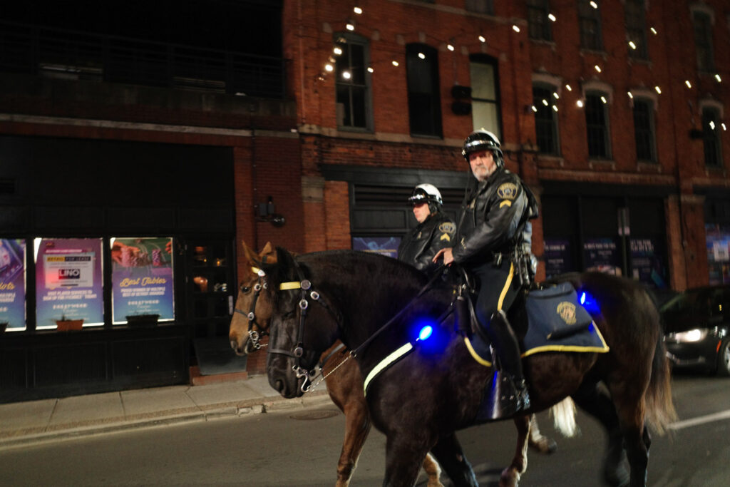 Two police officers on horseback at night in downtown Detroit.
