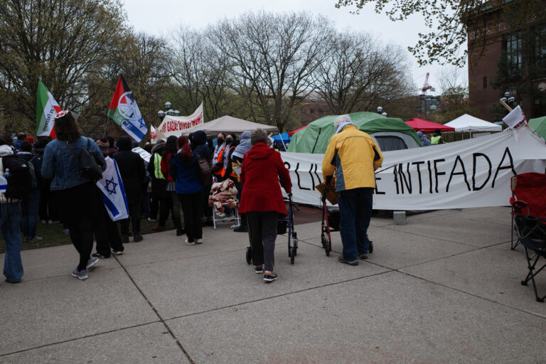 Protesters and counter protesters on the University of Michigan diag. Two old people with walkers. Palestine flags next to Israeli flags. Sign reading “Long Live the Intifada”