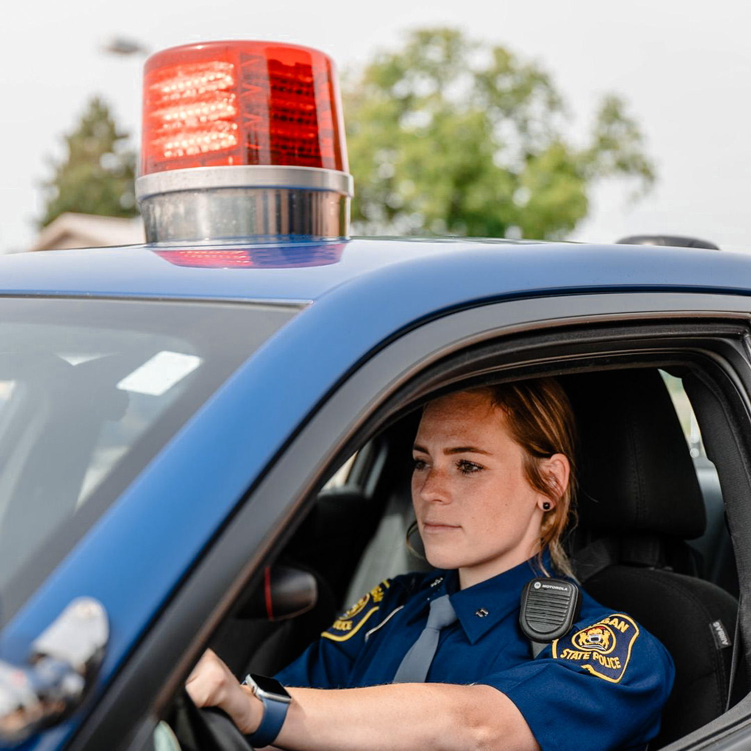 Faemale Michigan state police officer in patrol vehicle with red light on top flashing.