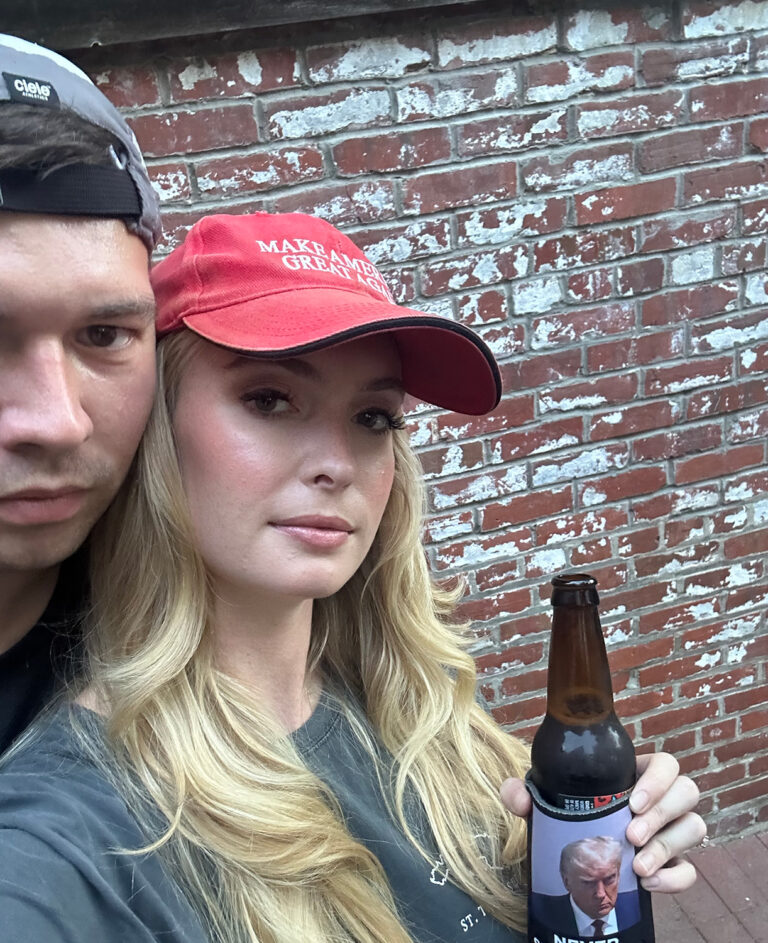 Blonde girl in MAGA hat holding beer.