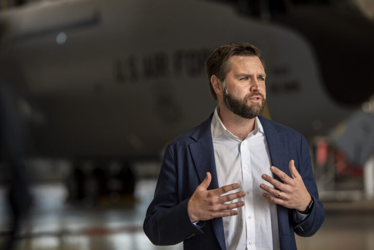 Senator J.D. Vance speaking with an Air Force cargo plane in background.