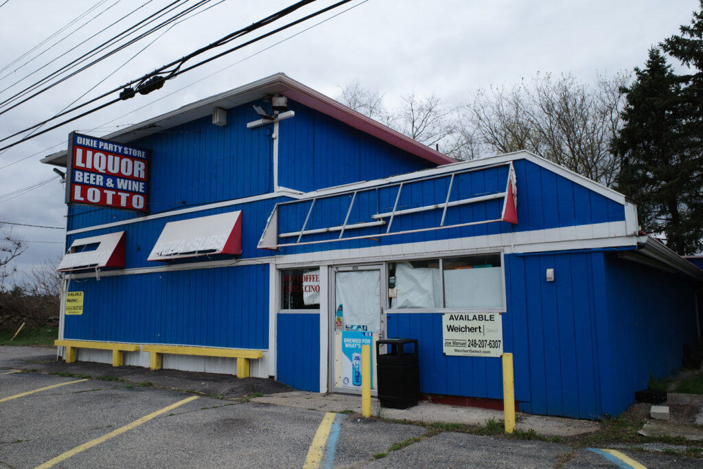 Abandoned blue “Dixie Party Store” with signs for “Liquor, Beer & Wine, Lotto” and a “For Sale” sign.