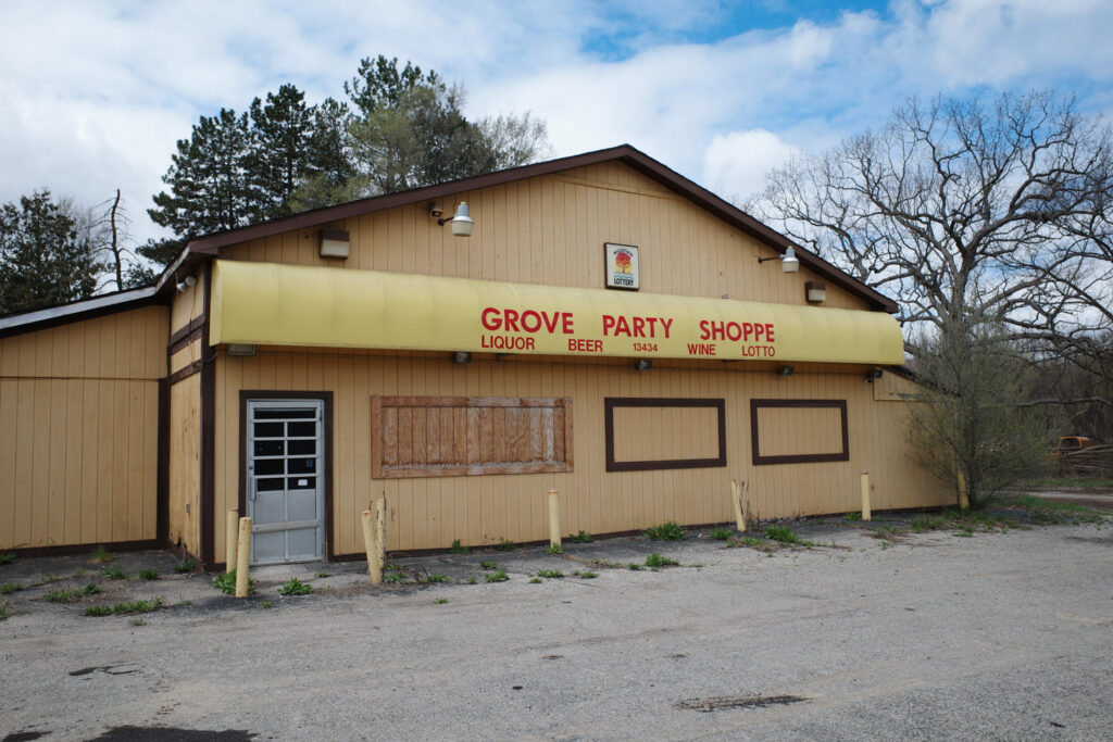 Abandoned yellow “Grove Party Shoppe” with boarded up windows and sign for “Liquor, Beer, Wine, Lotto”