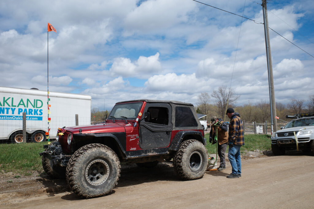 Muddy, red jeep on dirt road with men in flannel shirts checking it out.