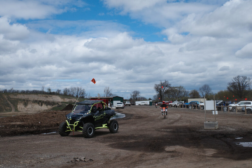 Side by side 4-wheeler and lone dirtbike traverse a dirt road heading towards the trails.
