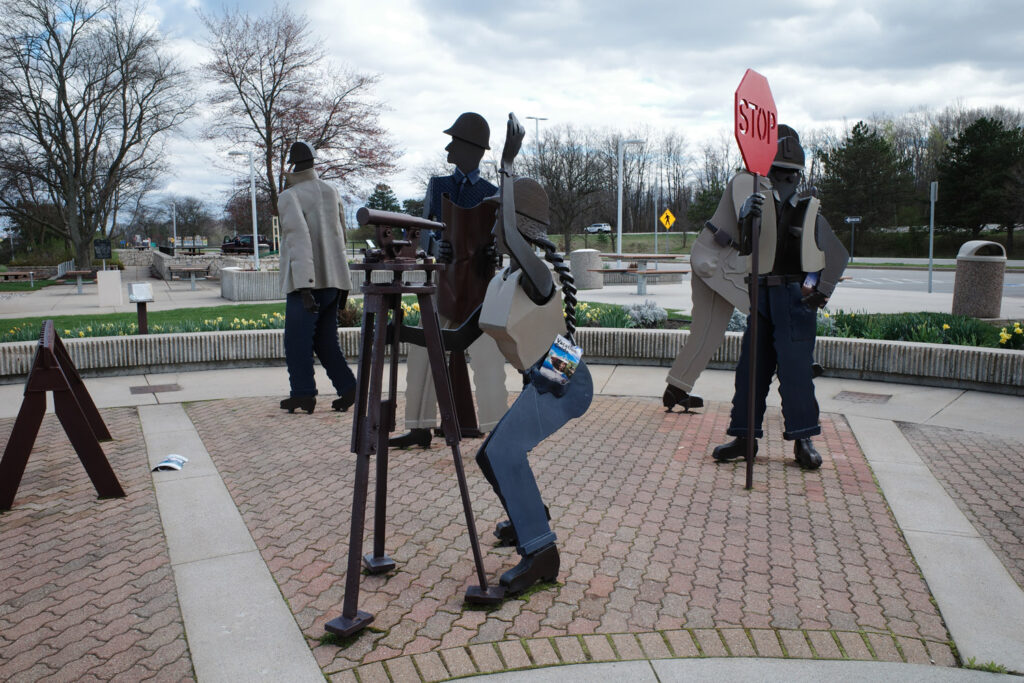 Steel metal sculptures of construction workers at highway rest stop in socialist neorealism style.