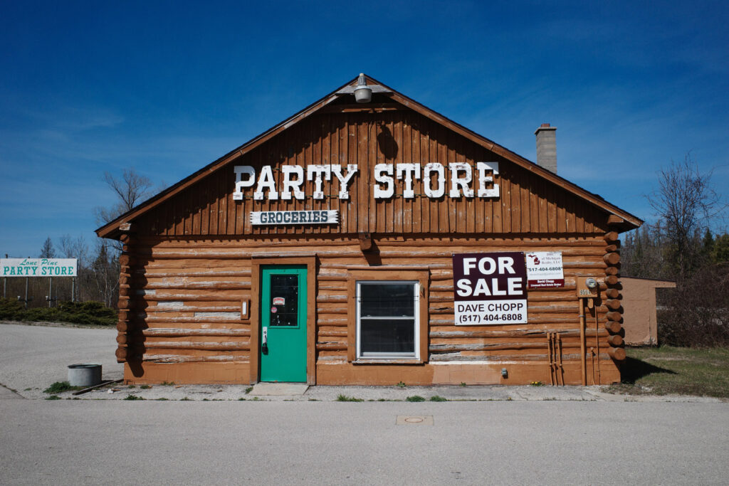 Cabin-style Party Store with signs saying “Party Store,” “Groceries,” and “For Sale.”