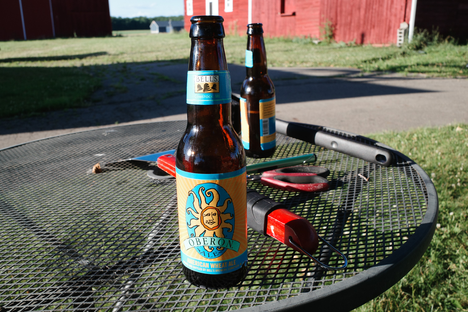 Two glass Oberon bottles on a metal table outside with grill equipment.