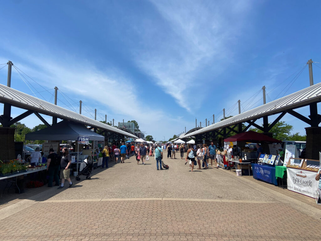 Photo of metal pavilions, tents and people visiting stalls at Holland Farmer’s market.