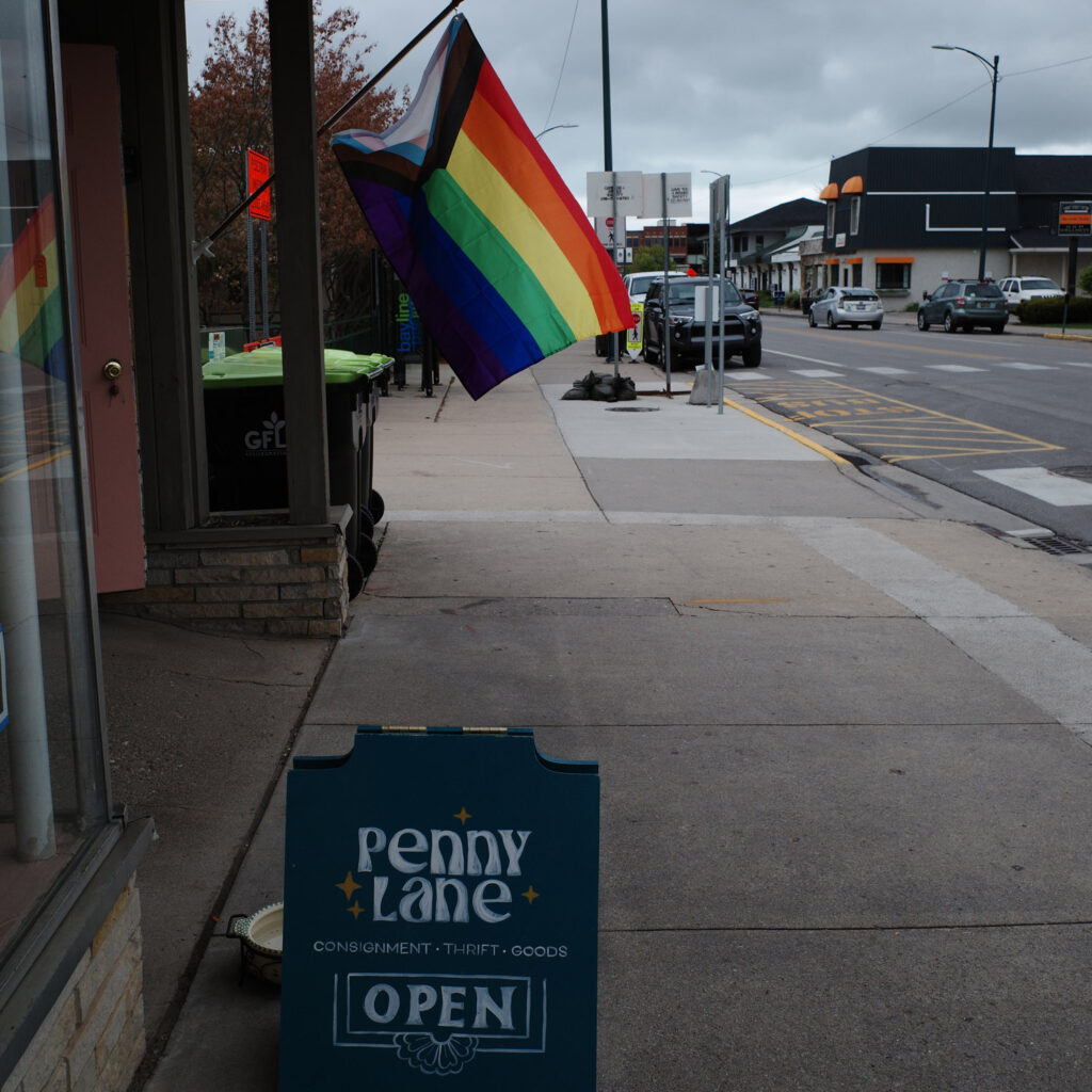 Progress Pride flag hanging out front of “Penny Lane” consignment shop.
