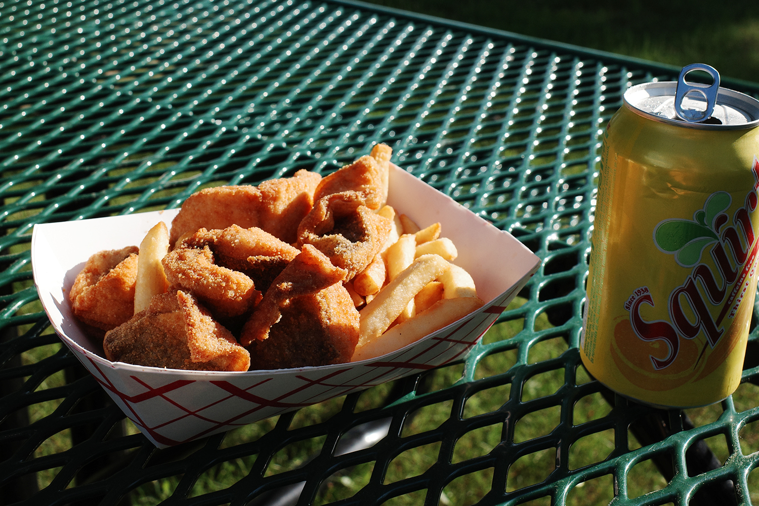 Fried fish and french fries in white container on outdoor table next to can of Squirt.