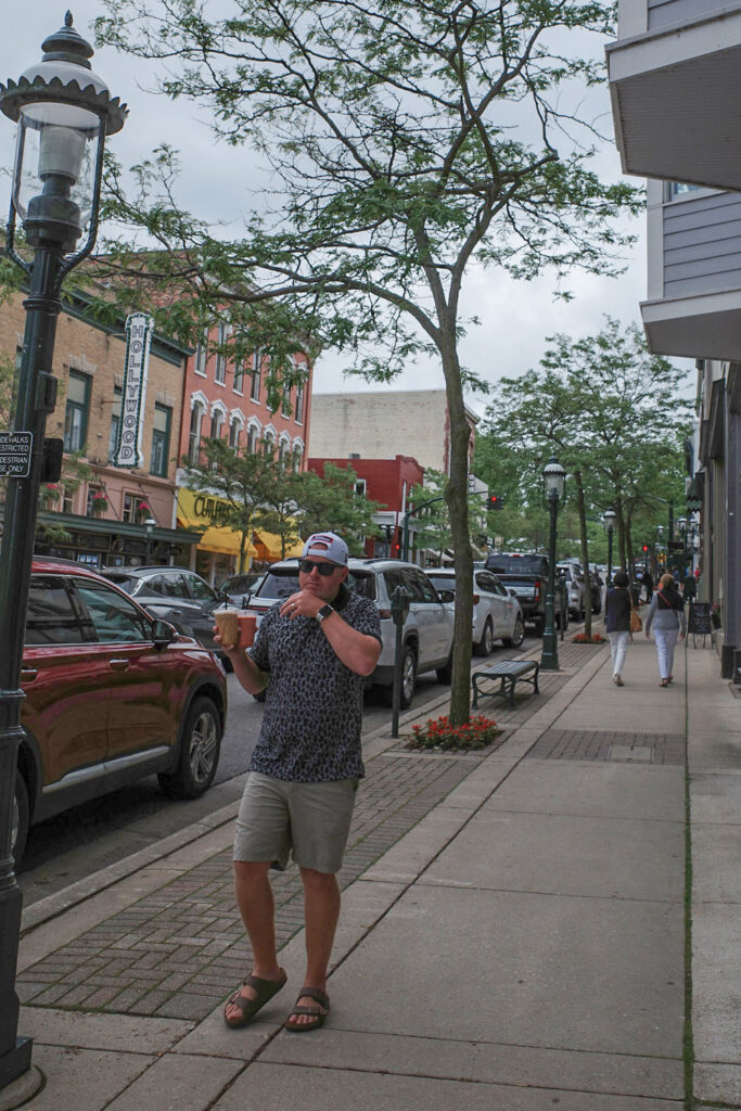 Man walking down a city street holding multiple iced coffee drinks in his hands.