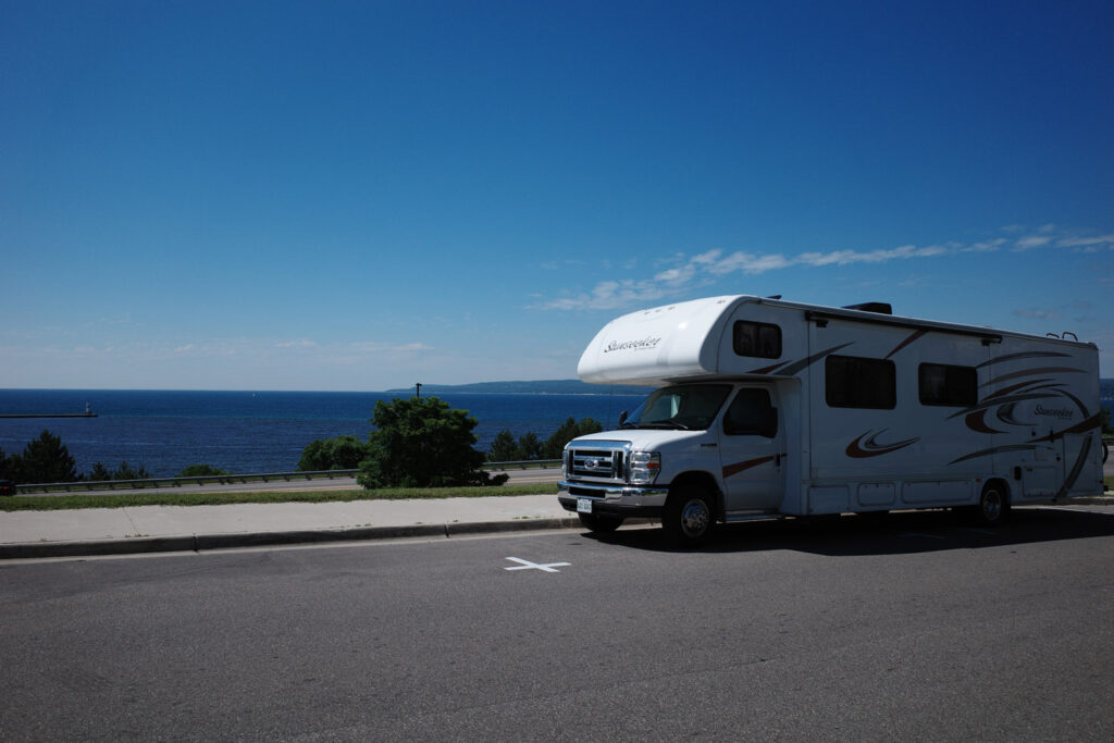 RV parked on side of road overlooking water.