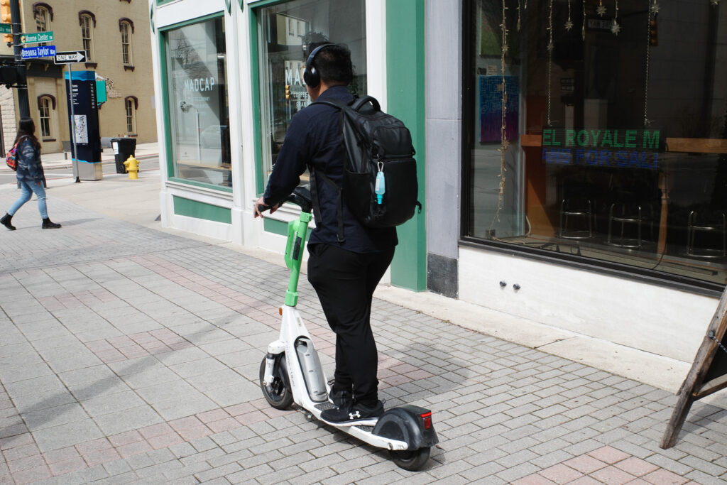 Man riding electric scooter on city sidewalk.