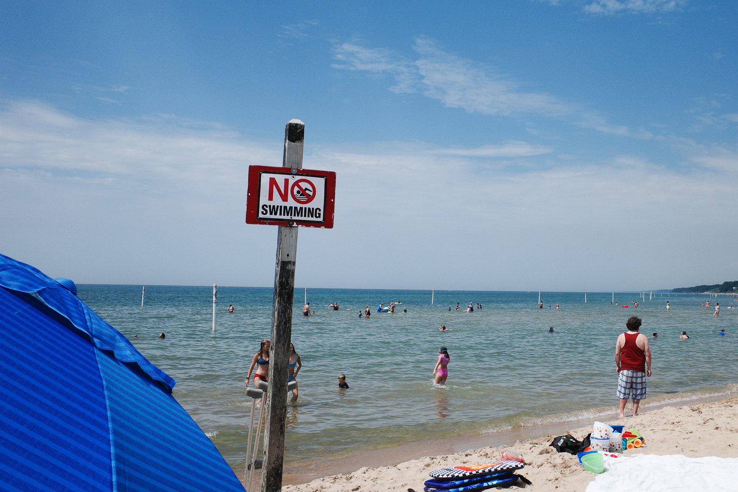 Sign saying “No Swimming” as swimmers swim in background.