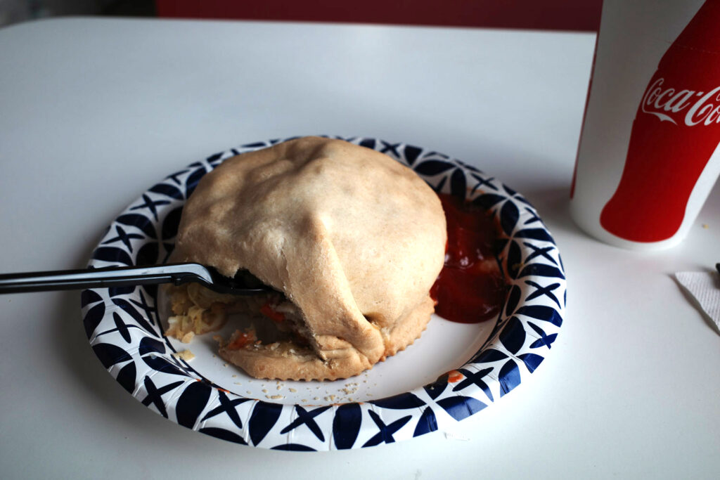 Pastie on plate with ketchup and coca-cola paper cup next to it.