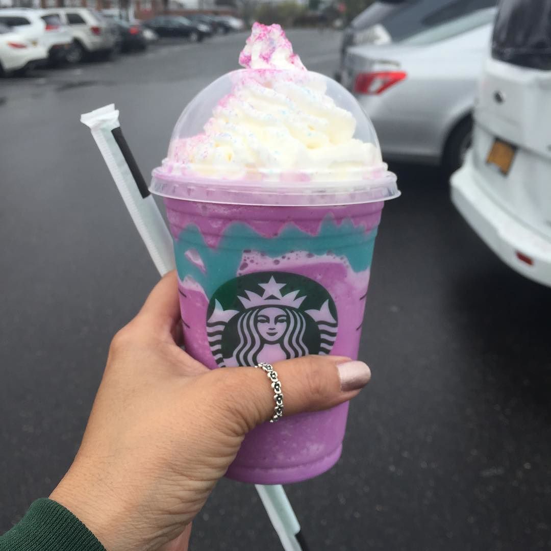 A hand holding a Starbucks Unicorn Frappucino with a straw.