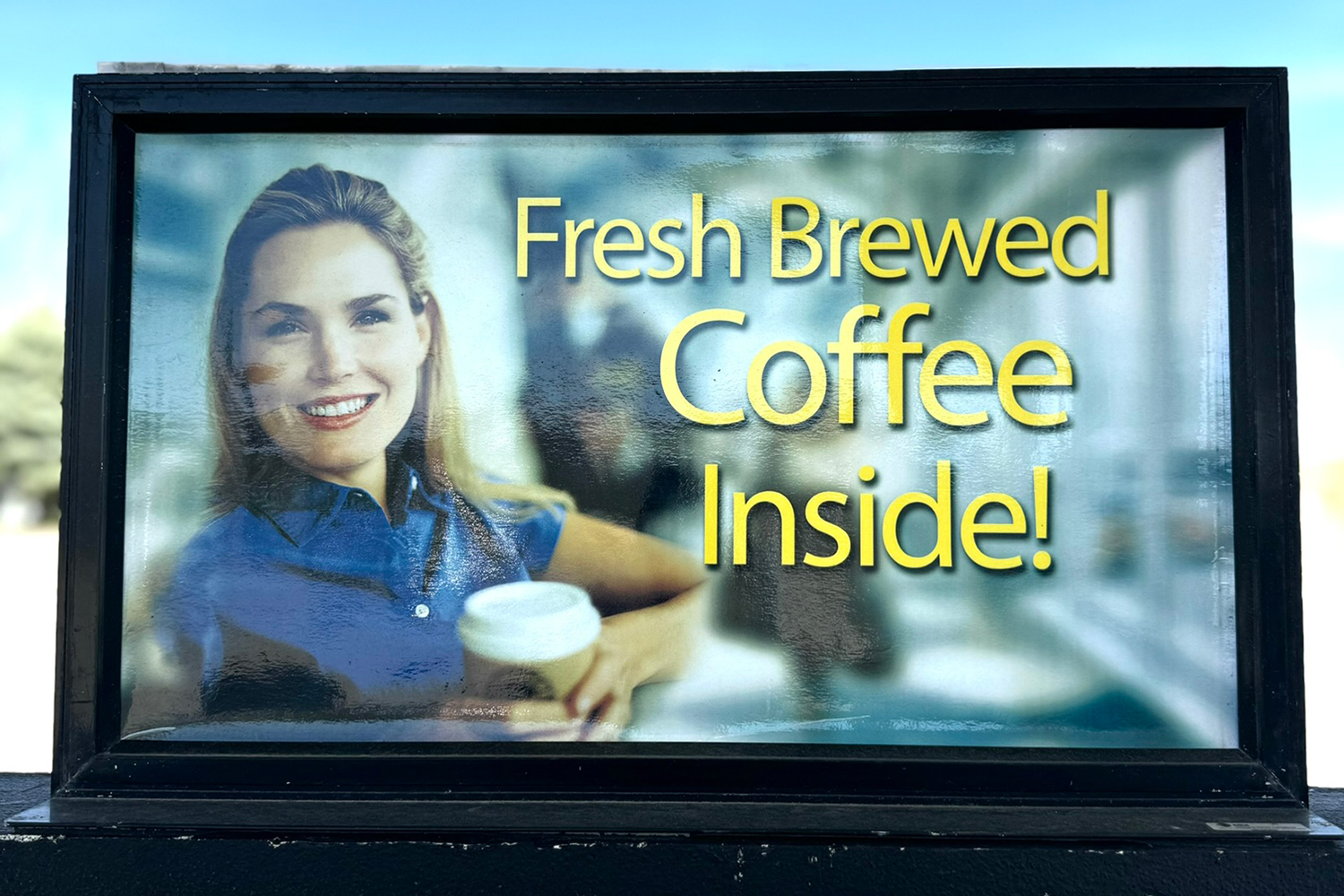 Sign with woman holding coffee cup advertising “fresh brewed coffee inside!”