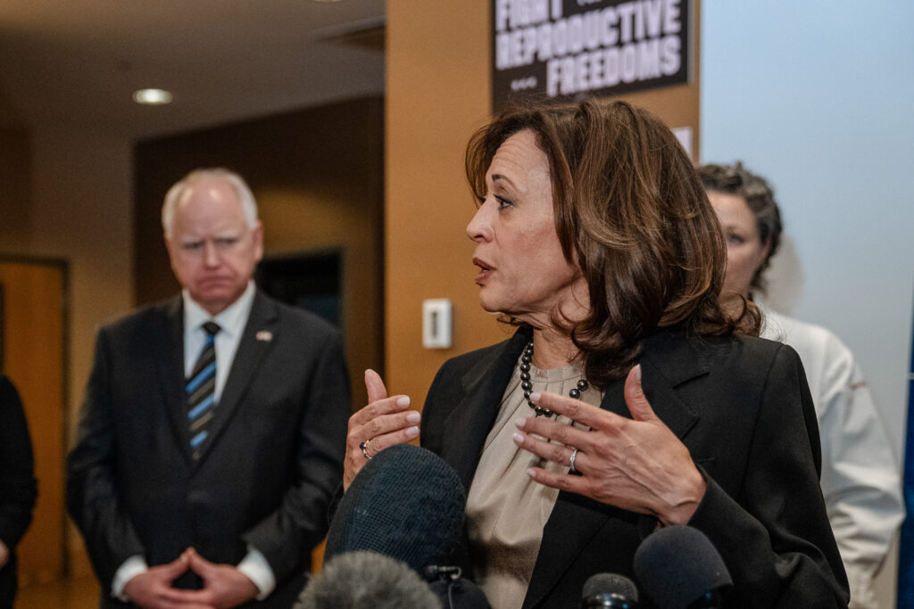 Kamala Harris speaking at podium with Tim Walz standing behind her.