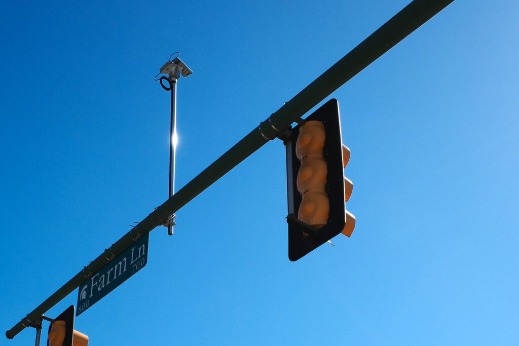 Camera above traffic lights on Farm Lane with MSU Spartan logo on street sign.