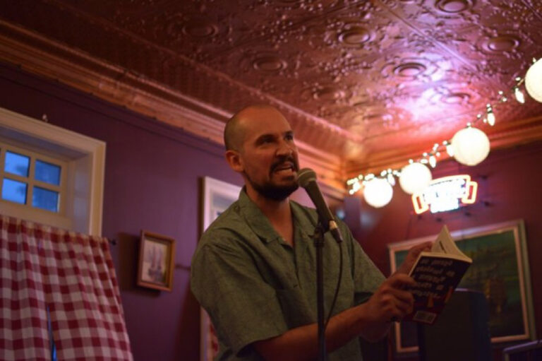 Man speaking into microphone with book at event.