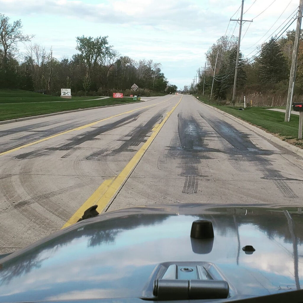 View from inside car looking down empty street with tire marks in front.