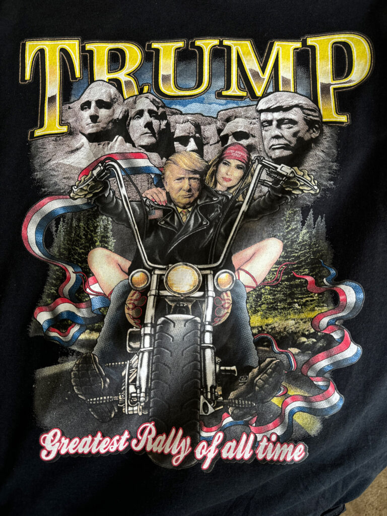 T-shirt with Trump on Mount Rushmore and riding chopper motorcycle with Melania in a MAGA hat on back reading "Trump" and "greatest rally of all time."