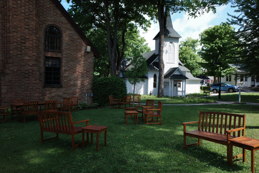 Wooden benches on shadowed lawn outside brick building and white chapel.