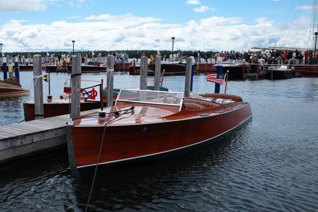 Wooden boat with old American flag docked in water with crowd in background.