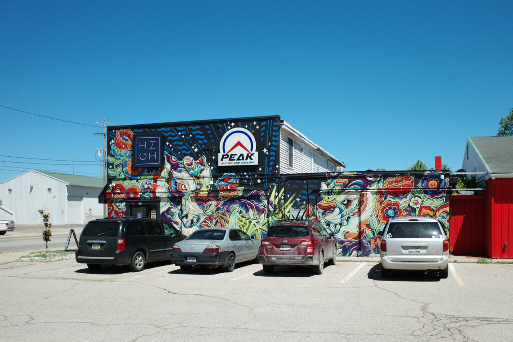 Exterior of “HIGH” cannabis dispensary with cars parked.