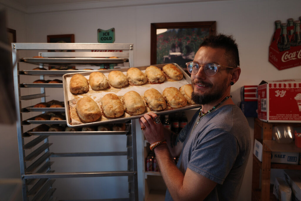 Man in glasses and beard holding tray of freshly baked pasties.