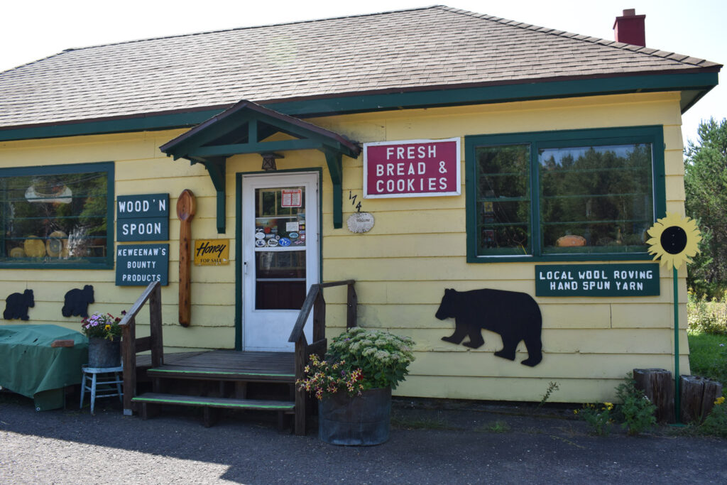 Wood'n Spoon store with signs reading "Wood'n Spoon" and "Keweenaw's Bounty Products" and "fresh bread and cookies" and "local wool roving hand spun yarn"