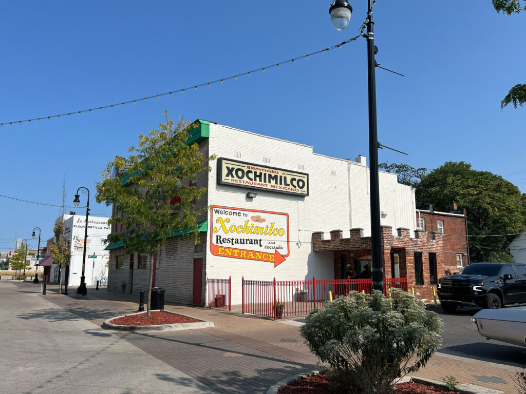 Outside of Xochimilco restaurant with white painted brick facade and sign reading "Welcome to Xochilmico restaurant, and cocktails, entrance"