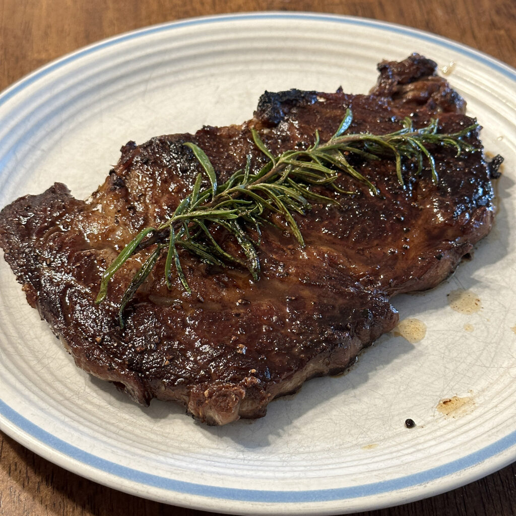 Steak on plate with rosemary on top.