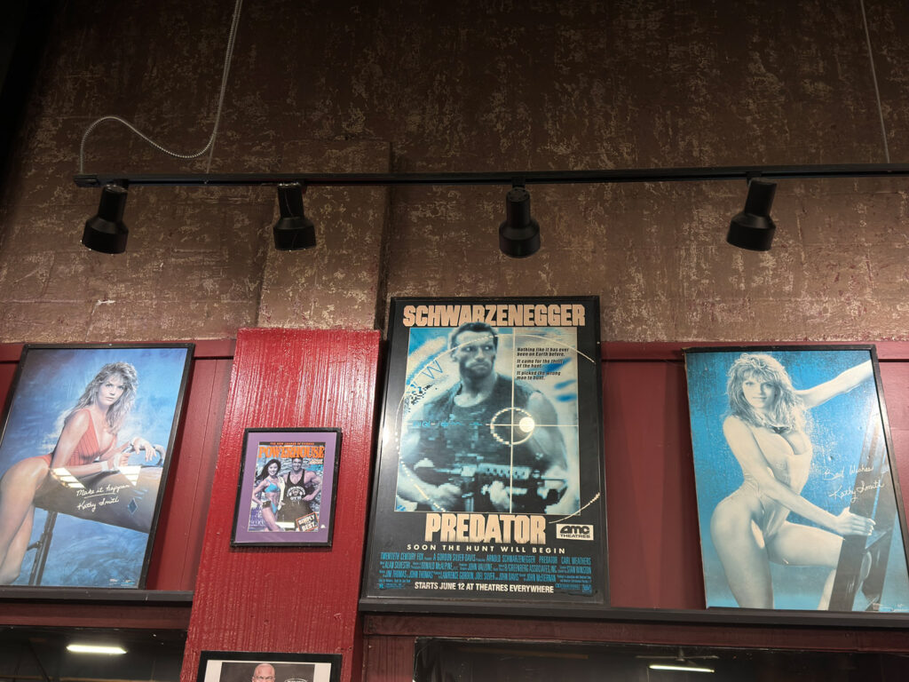 Movie poster for Predator featuring Arnold Schwarzenegger, flanked by posters of female bodybuilders.