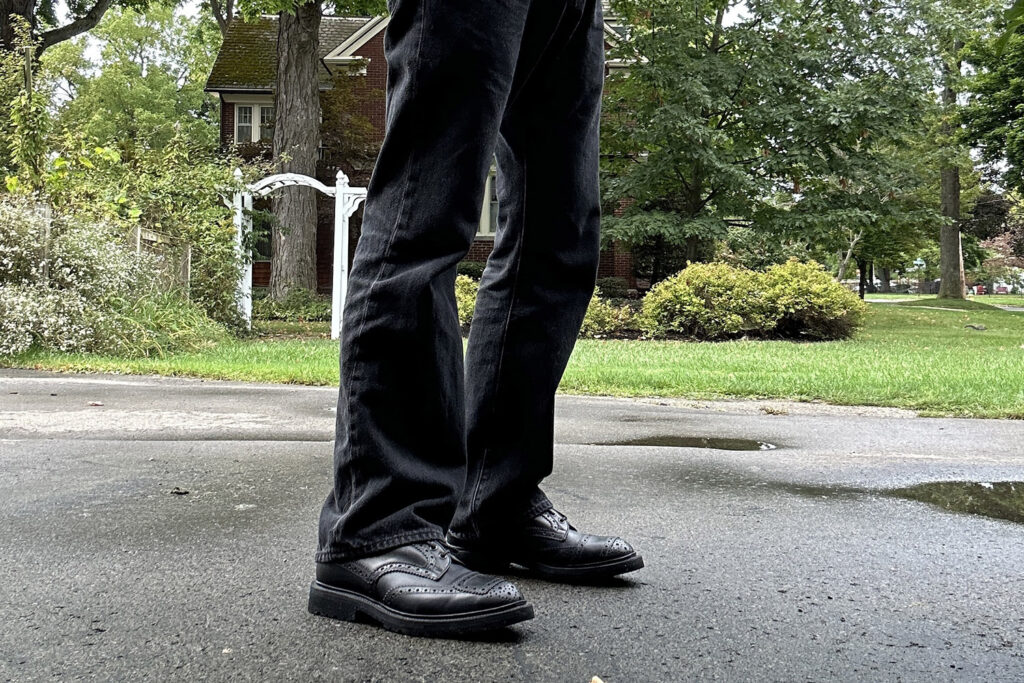 Closeup of black bootcut jeans silhouette on man standing in driveway.