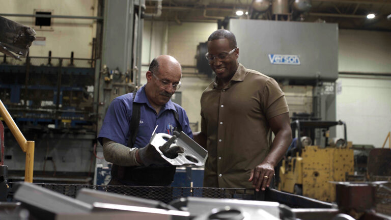 Rep. John James in factory warehouse with worker admiring steel products.