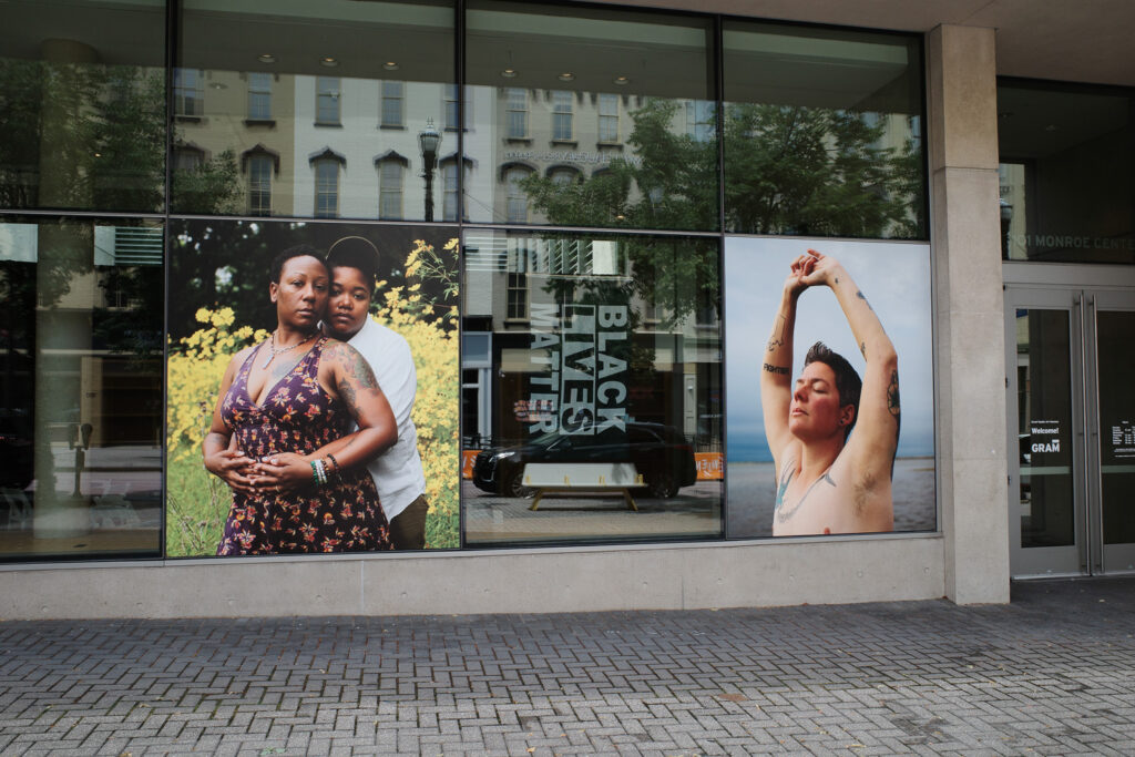 Outside the GRAM, two photographs of a black lesbian couple and a person with top surgery scars.