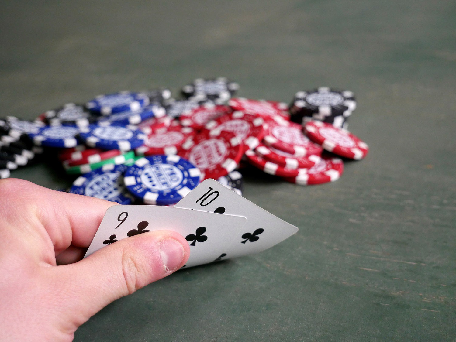 Man showing cards, 10 and 9 of clubs, next to poker chips.