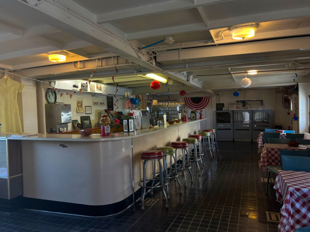 Bar with stools inside ship with sign reading "Soda Bowl"