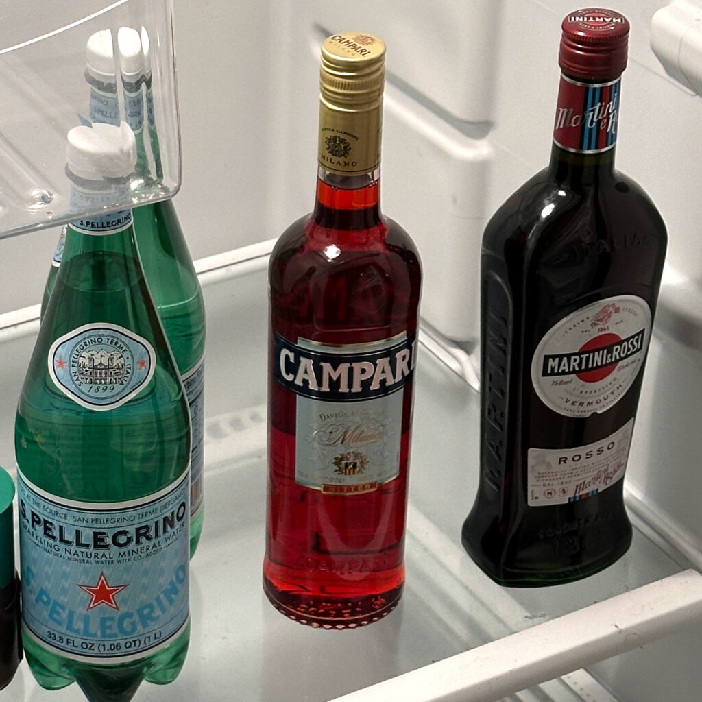 Bottle of Campari in fridge next to vermouth and san pellegrino.