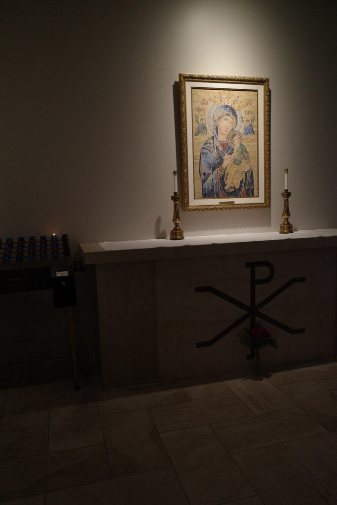 Icon of the Virgin Mary and Jesus next to candles in church.