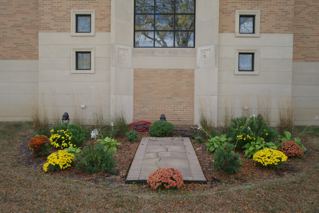 Flower beds outside church with etching in stone reading "Church of the Holy Family"